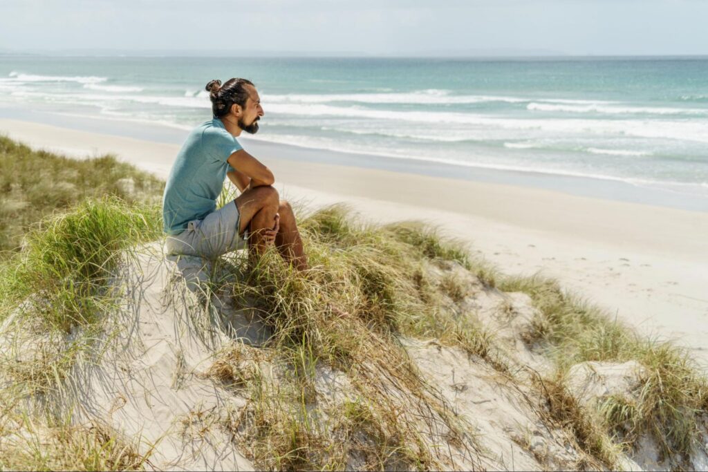 Dispirited man sitting on beach gazing at sea